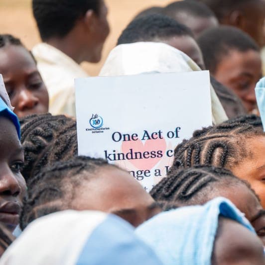 Schoolgirls with a KHI "One Act of Kindness" sign at a school outreach